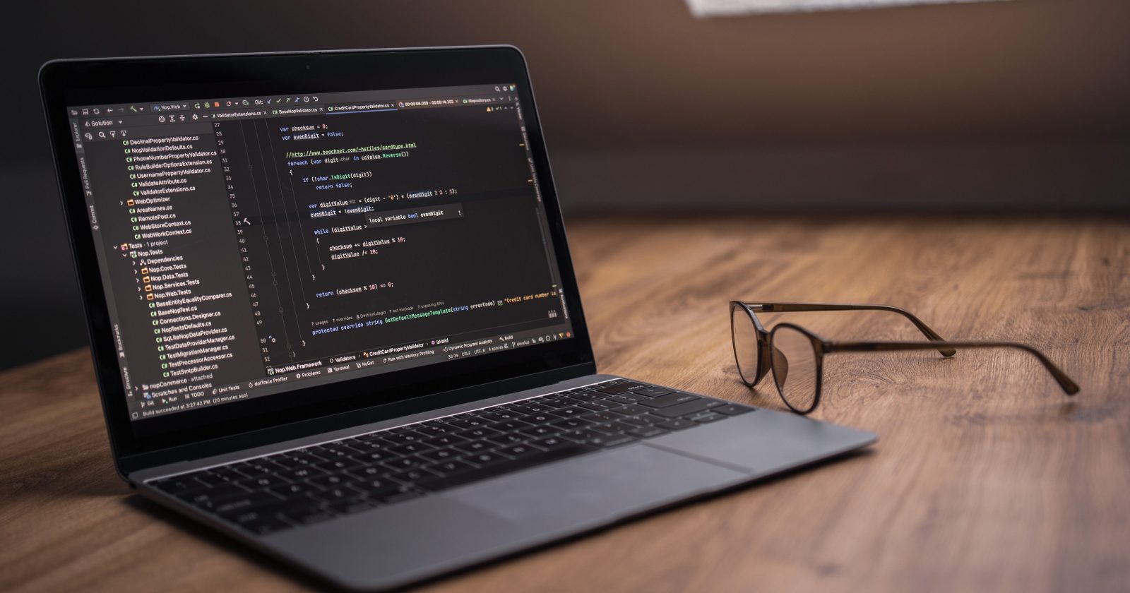 Portátil con un editor de código abierto sobre un escritorio de madera, junto a unas gafas